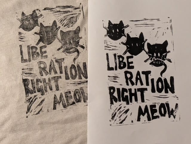 Linocut print in black on cloth and paper of a design with cats holding a rat and the words LIBE RAT TION RIGHT MEOW