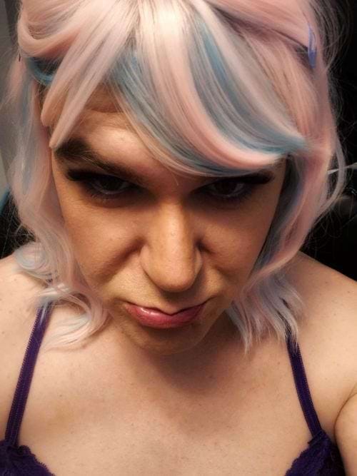 white transfem with pale pink and blue bangs and shoulder-length hair pinned with barrettes, head tilted down and looking at camera