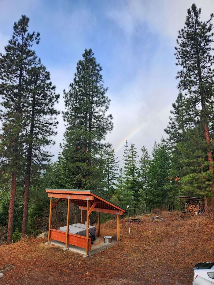 view overlooking hot tub with trees behind and a rainbow in the sky