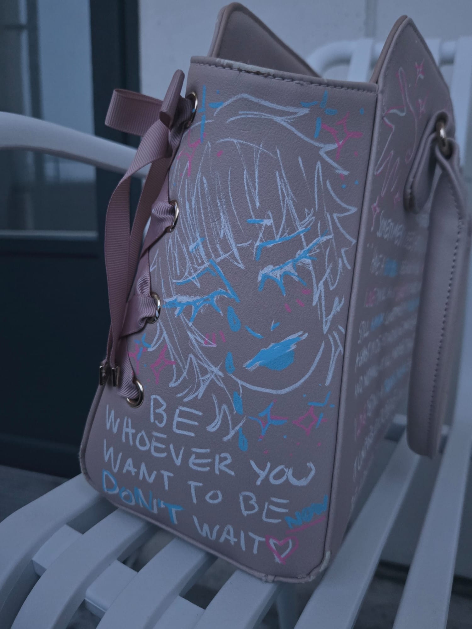 gray bag covered in white blue and pink sketches of a crying and smiling anime face and writing saying Be Whoever You Want to Be Don't Wait